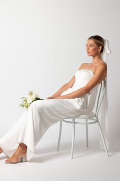 a woman is sitting on a chair with a flower in her hand and wearing a white dress