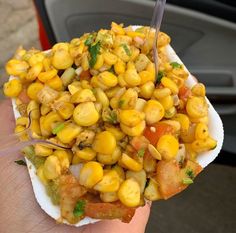 a person holding a paper plate with corn on it