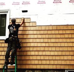 a man on a ladder painting the side of a house that is being built with wood shingles