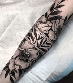 a black and white tattoo with flowers on the arm, done by an experienced artist