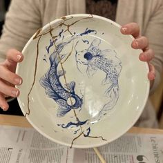 a woman holding up a plate with a fish design on the front and side of it