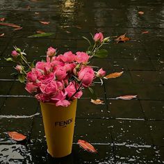 a yellow vase filled with pink flowers on top of a wet ground