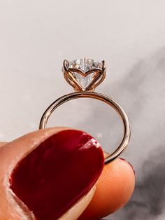 a hand holding a ring with a diamond on it's side and a red lip