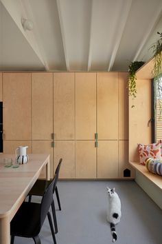 a cat sitting on the floor in front of a dining room table with chairs and cupboards