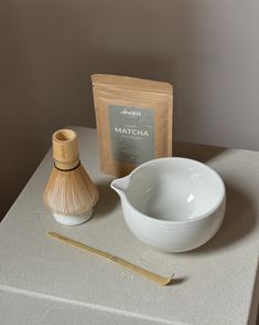 a white bowl and wooden spoon sitting on top of a counter next to a bag of matcha