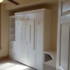 an empty room with white cupboards and shelves in the corner, next to a ceiling fan