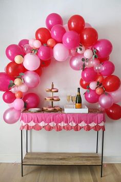 a table topped with lots of pink and red balloons next to a wine glass filled bottle