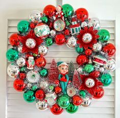 a wreath made out of christmas ornaments on a window sill in front of a white door