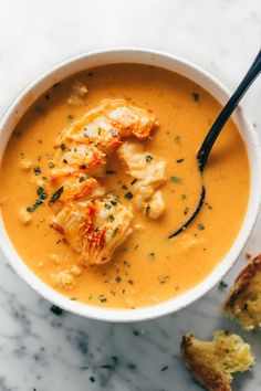 a white bowl filled with soup on top of a marble counter next to bread pieces