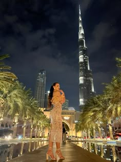 a woman standing in front of the burj tower at night with palm trees