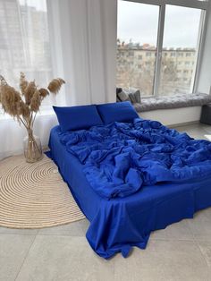 a large blue bed sitting in the middle of a living room next to a window