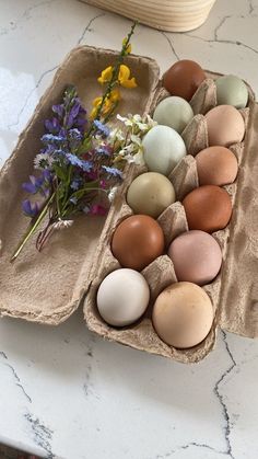 an egg carton filled with eggs on top of a white counter next to flowers