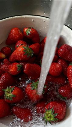 strawberries are being washed in a large bowl