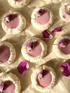 several cookies with pink icing and rose petals on them sitting on wax paper next to each other