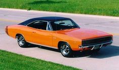 an orange and black muscle car parked on the side of the road next to grass