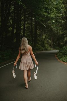 a woman walking down the middle of a road holding two umbrellas in her hand