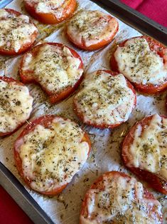 tomatoes with cheese and seasoning sitting on a baking sheet