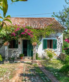 an old house with green shutters and pink flowers on the front door is surrounded by greenery