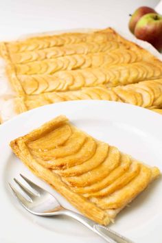 a piece of apple pie on a plate with a fork next to it and an apple in the background