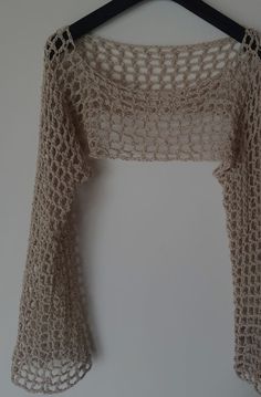 a crocheted top hanging on a hanger next to a white wall,