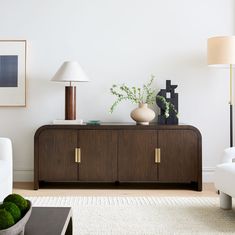 a living room with white couches and green plants on top of a wooden cabinet