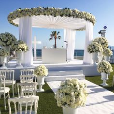 an outdoor wedding setup with white chairs and flowers on the aisle, overlooking the ocean