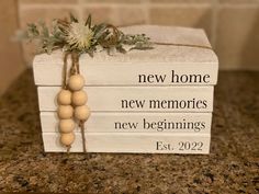 a wooden box with some wood beads tied to it and the words new home, new memories, new beginnings