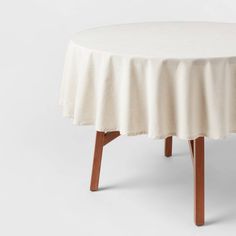 a round table with wooden legs and a white cloth draped over the top, on a white background