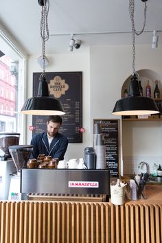 a man working behind the counter at a coffee shop with two hanging lights above him