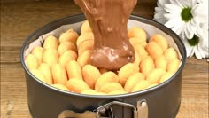 a person pouring chocolate into a tin filled with donuts