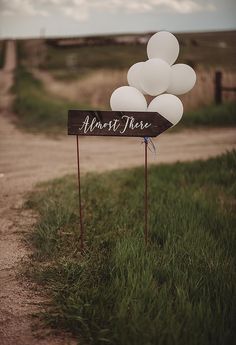 there is a sign with balloons on it that says almost there in front of some grass