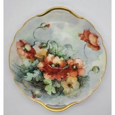 a plate with flowers painted on it and gold trimming around the edge, sitting on a white surface