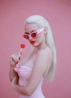 a woman with white hair wearing sunglasses and holding a lollipop in her hand