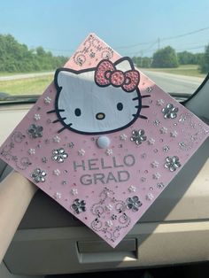 a pink hello kitty graduation cap sitting on the dashboard of a car with silver sequins