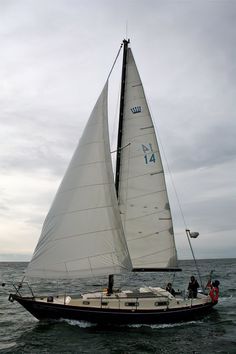 a sailboat with white sails is in the open water on a cloudy, overcast day