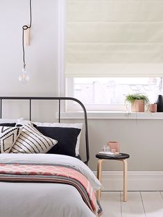 a bedroom with white walls, black and white bedding, pink throw pillows and an iron frame headboard