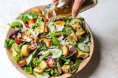 someone pouring dressing onto a salad in a bowl