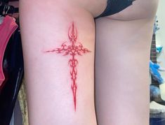 a cross tattoo on the back of a woman's thigh is shown in red ink