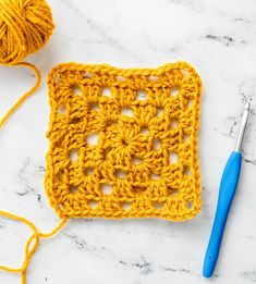 the crochet square is next to a pair of knitting needles and a ball of yarn