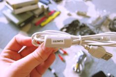 a hand holding a white cord with the word camera on it in front of many other wires