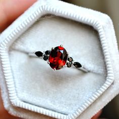 a close up of a ring with a red stone in it on a white box