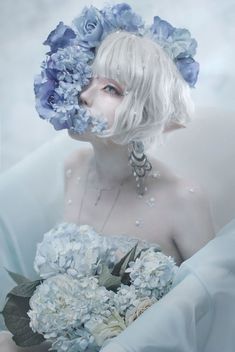 a woman with white hair and blue flowers in her hair is holding a bouquet of hydrangeas