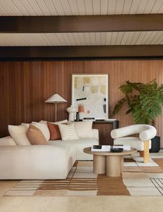 a living room with wood paneling and white couches, coffee table and lamp