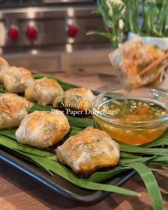 some food is sitting on a plate with green leafy leaves and dipping sauce in a bowl