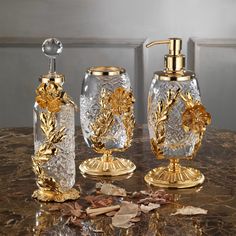 three pieces of glass with gold accents on a marble counter top, including soap dispenser and toothbrush holder