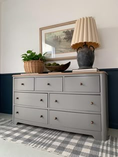 a dresser with two vases on top of it and a lamp in the corner