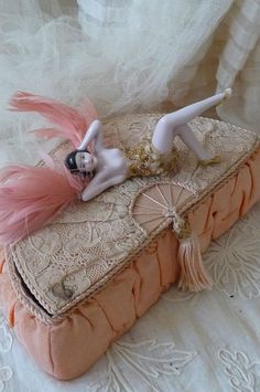 a doll is laying on top of an old book with pink feathers and lace around it