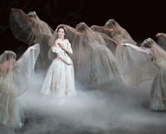 a woman in white dress standing on stage surrounded by veils