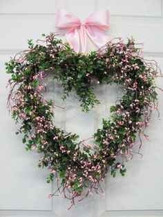 a heart shaped wreath with pink flowers and greenery hanging on the wall in front of a door