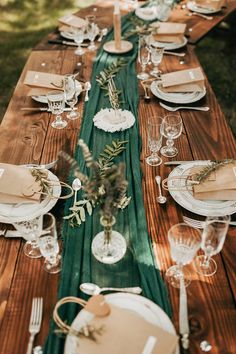 a long wooden table with place settings and plates on it is set for an outdoor dinner